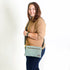 Woman wearing a beige shirt and blue jeans with a green crossbody bag on a white background
