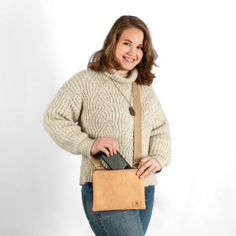 Woman wearing a beige sweater holding a tan crossbody bag against a white background