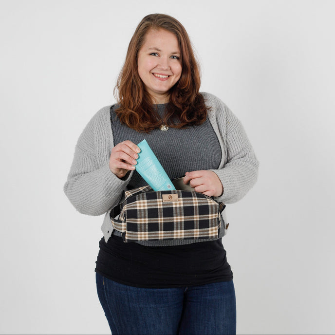 Woman holding a blue lotion bottle with a plaid-patterned toiletry kit on a white background