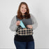 Woman holding a blue lotion bottle with a plaid-patterned toiletry kit on a white background