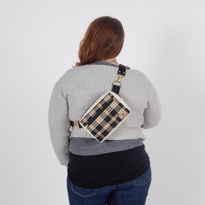 Person wearing a plaid crossbody bag on a plain background