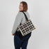 Woman carrying a plaid bag over her shoulder on a plain background
