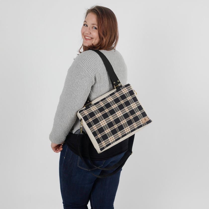 Woman carrying a plaid bag over her shoulder on a plain background