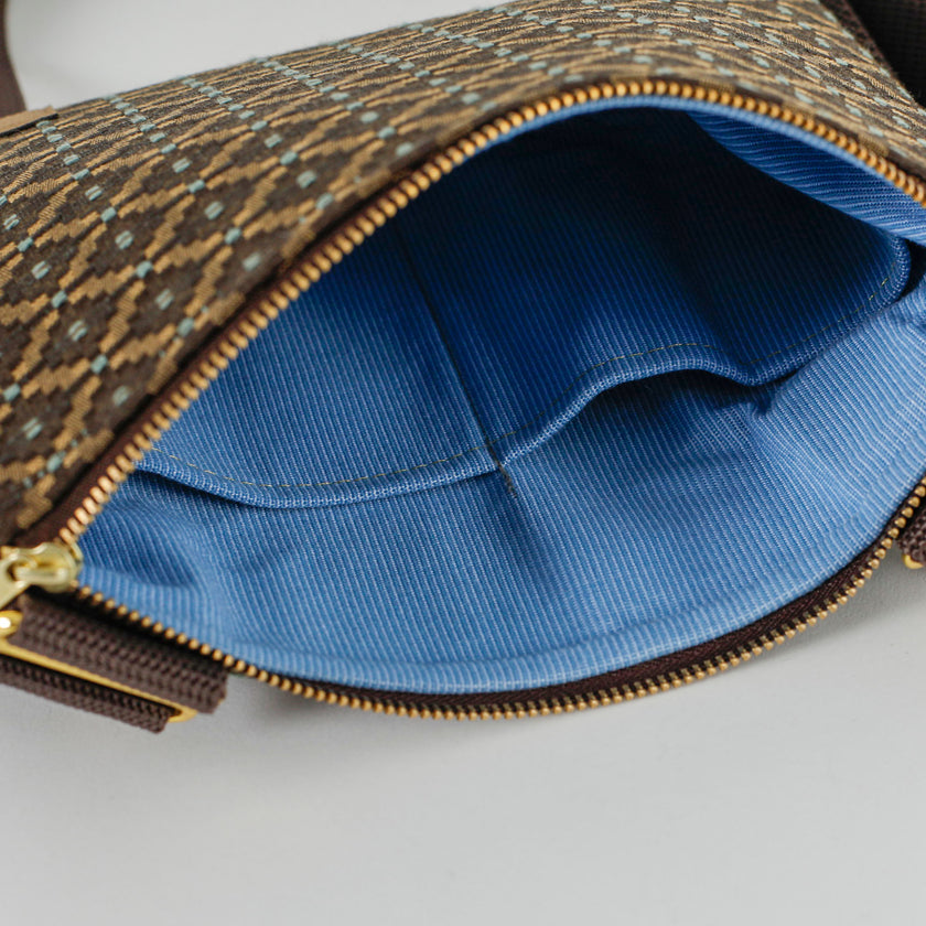 Open brown and blue geometric print fabric crossbody pouch with blue striped fabric interior on a white background