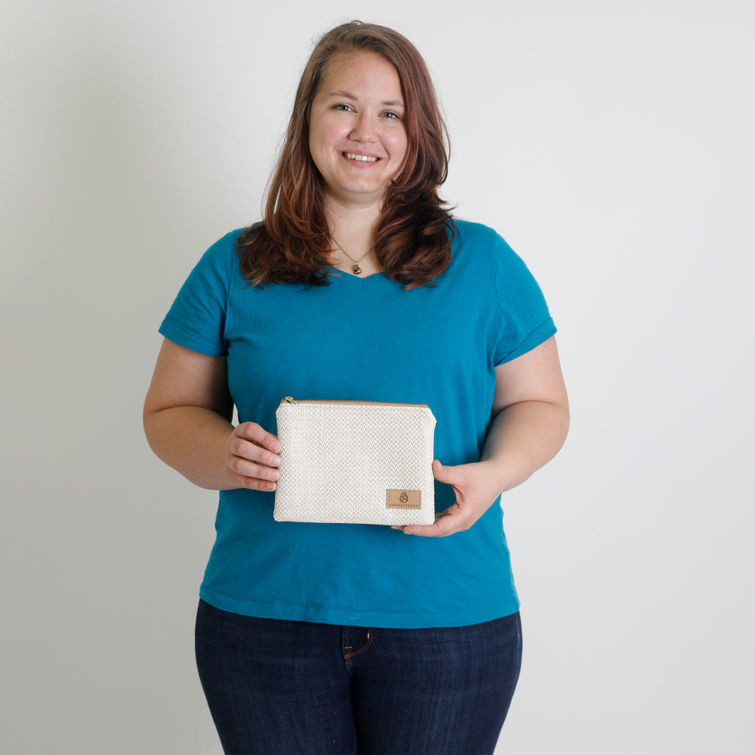 Woman holding a white pouch with a tan logo against a plain background