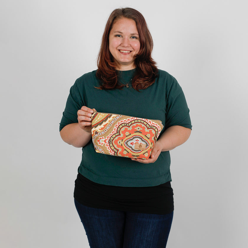 Woman holding a patterned makeup bag against a plain background