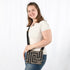 Woman holding a black and brown geometric patterned crossbody pouch against a white background