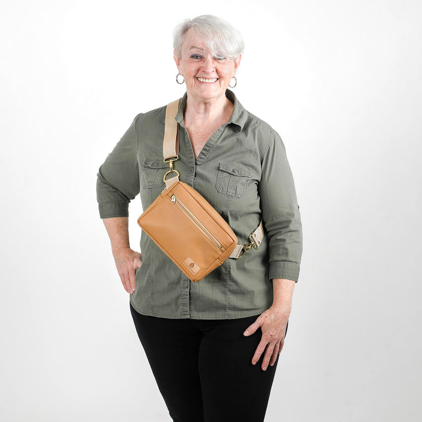 Woman wearing a green shirt and black pants with a tan crossbody bag on a white background