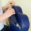 Blue heart bag handcrafted from upcycled Southwest airlines seat leather with gold zipper being held by a person against a plain background