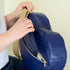 Blue heart bag handcrafted from upcycled Southwest airlines seat leather with gold zipper being held by a person against a plain background