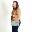 Woman wearing a beige shirt and blue jeans with a green crossbody bag on a white background