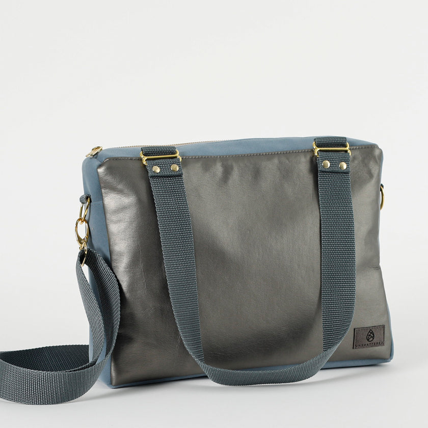 A charcoal  and blue convertible handbag with gold-tone hardware, an adjustable crossbody strap, and a floral patterned interior.