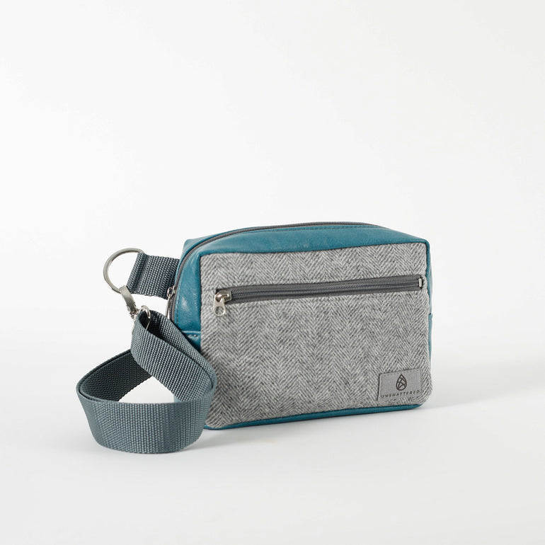 A small crossbody bag with teal luxury leather alternative and gray wool fabric, featuring a front zip pocket and an adjustable cotton strap.