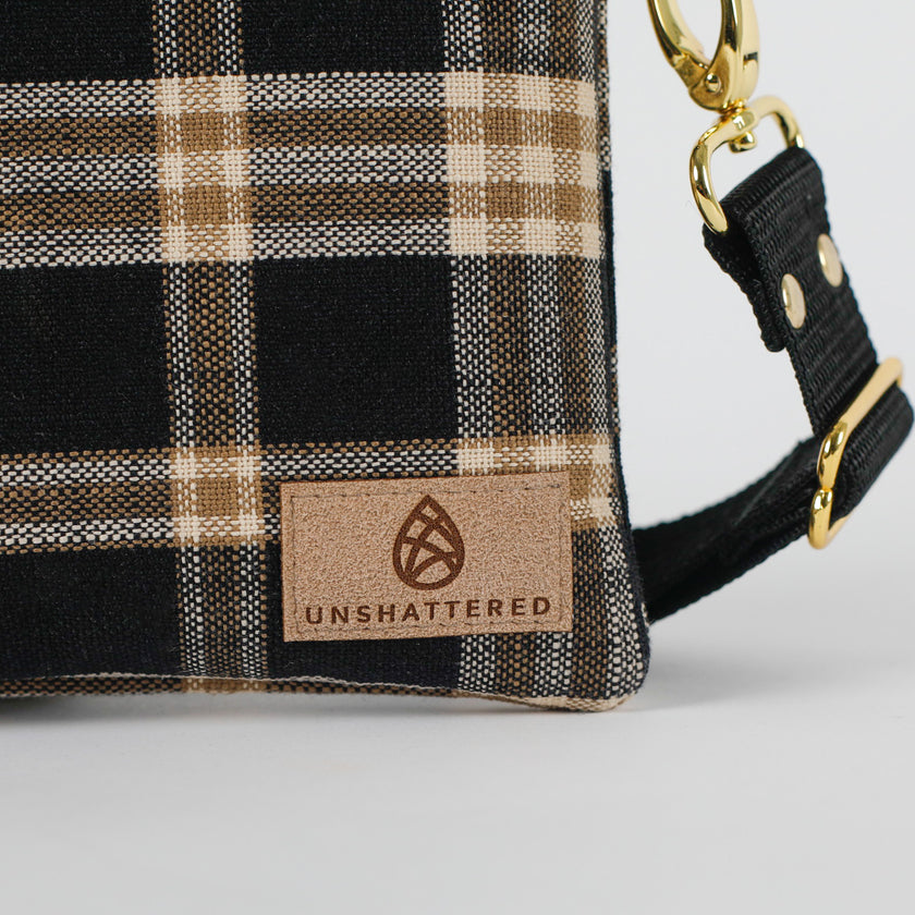 Plaid bag with 'Unshattered' brand logo on a white background