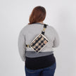 Person wearing a plaid crossbody bag on a plain background