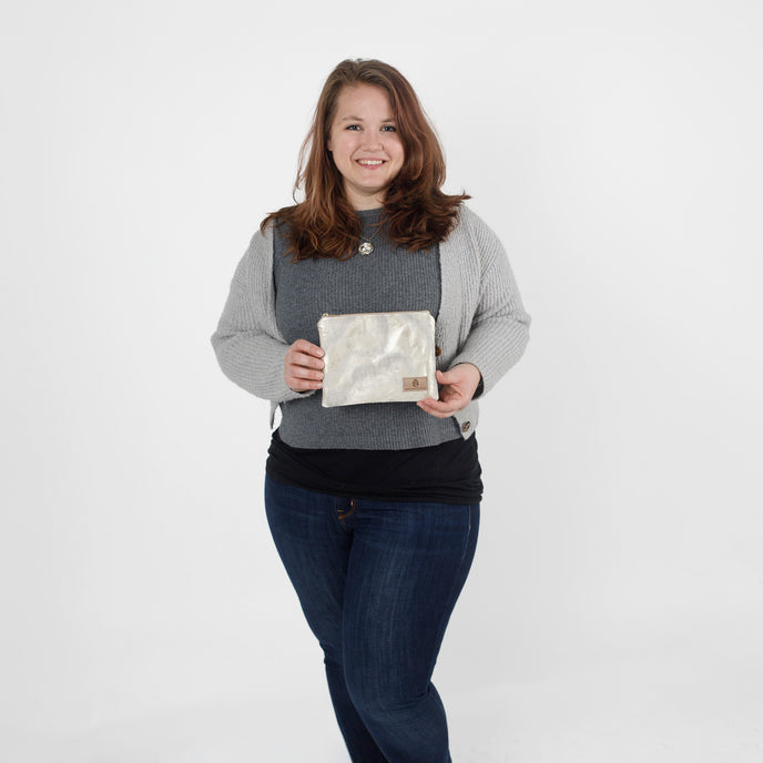 Woman holding a zip pouch handcrafted from upcycled materials  against a white background