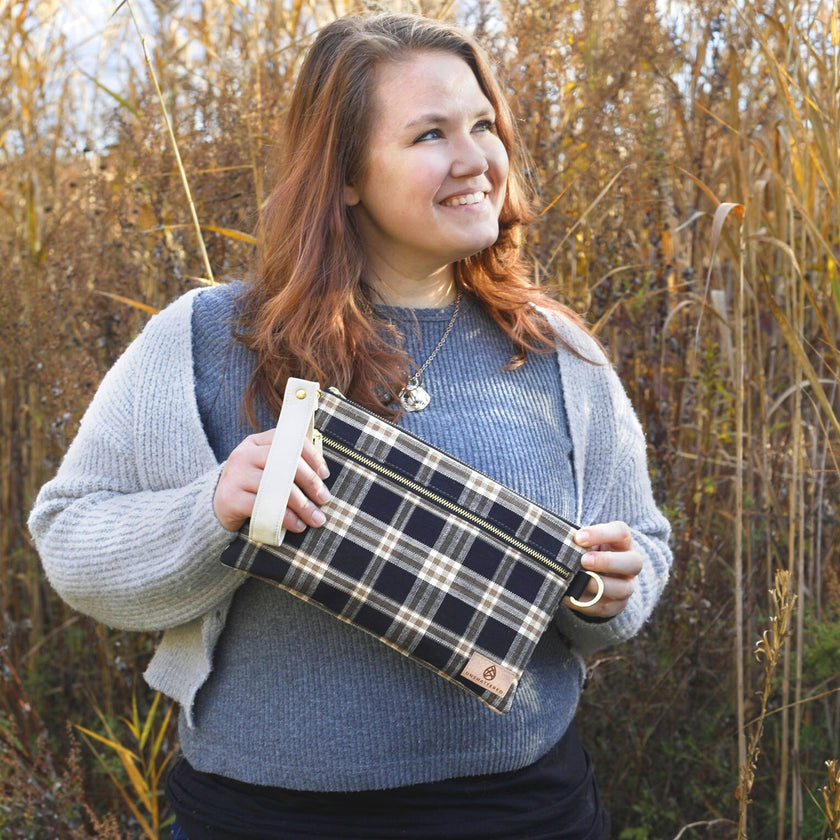 Woman holding a plaid bag in front of tall grass