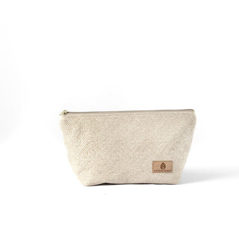 A beige, textured makeup bag named Theresa with a zip closure and a suede Unshattered label on a white background