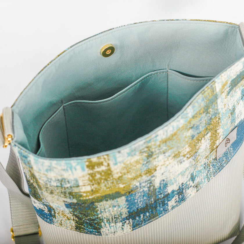 A blue fabric interior with gold snap button on a blue, green and white tote bag with gray outdoor furniture on the bottom