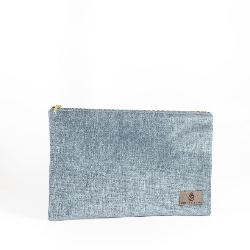 A blue velvet large zip pouch named after Laura with gold-tone hardware, featuring a suede Unshattered label.