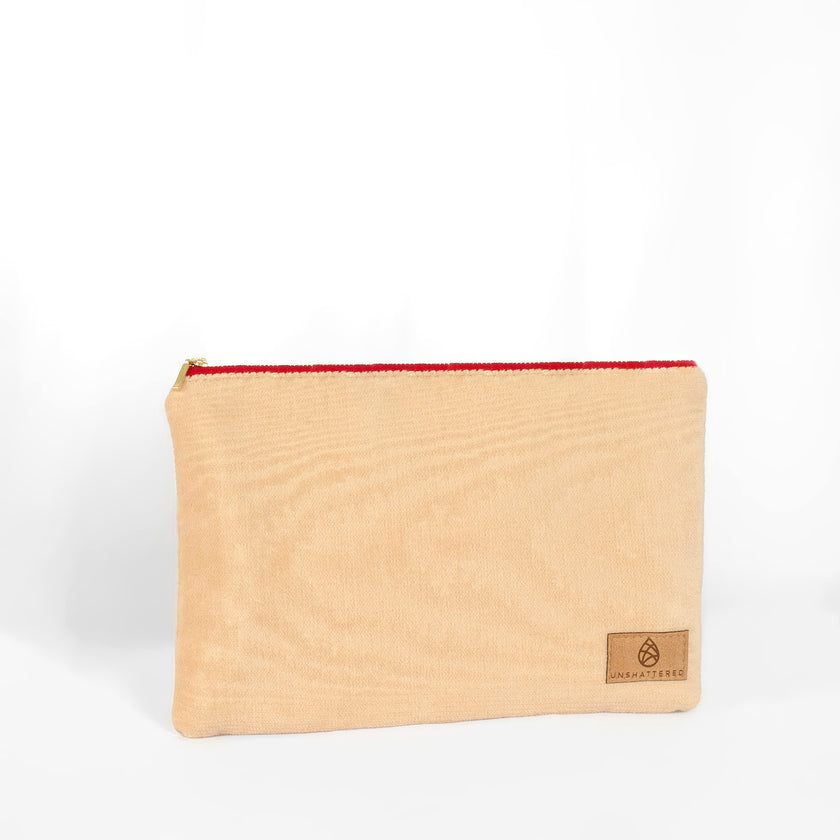 A large zip pouch made with soft, neutral upcycled fabric, featuring a red zipper and a brand tag displaying Unshattered