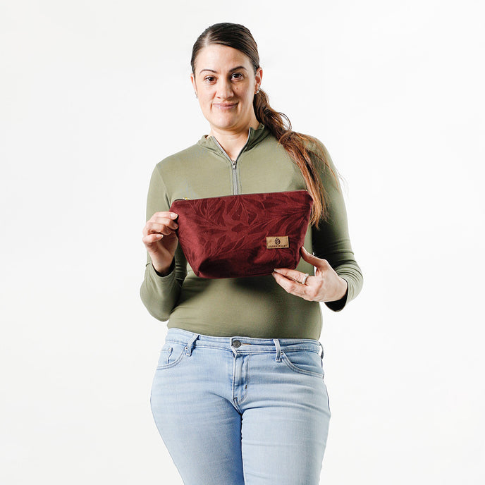 A woman holding a burgundy makeup bag with a burgundy leaf design