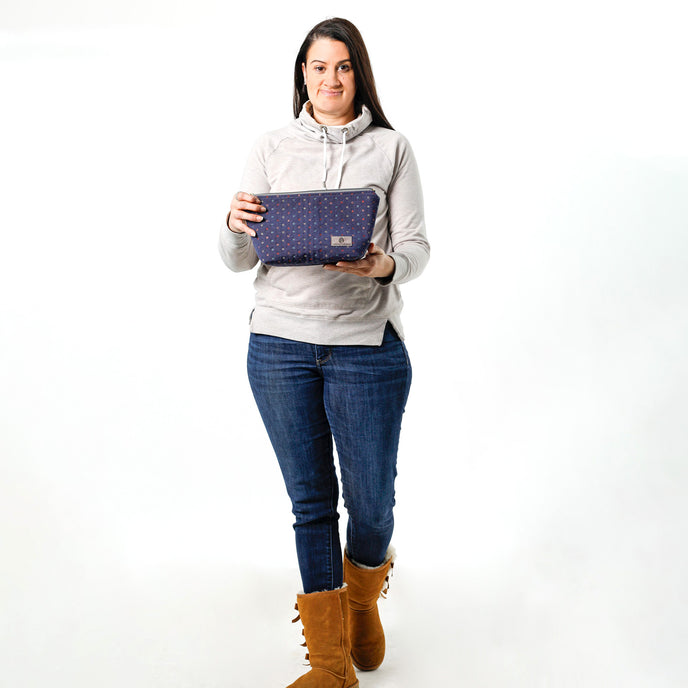 A woman holding a dark blue makeup bag made from upcycled fabric reclaimed from an interior designer
