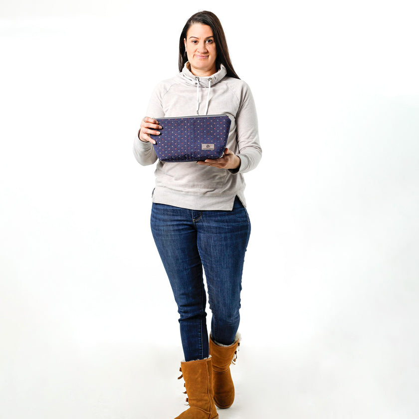 A woman holding a dark blue makeup bag made from upcycled fabric reclaimed from an interior designer