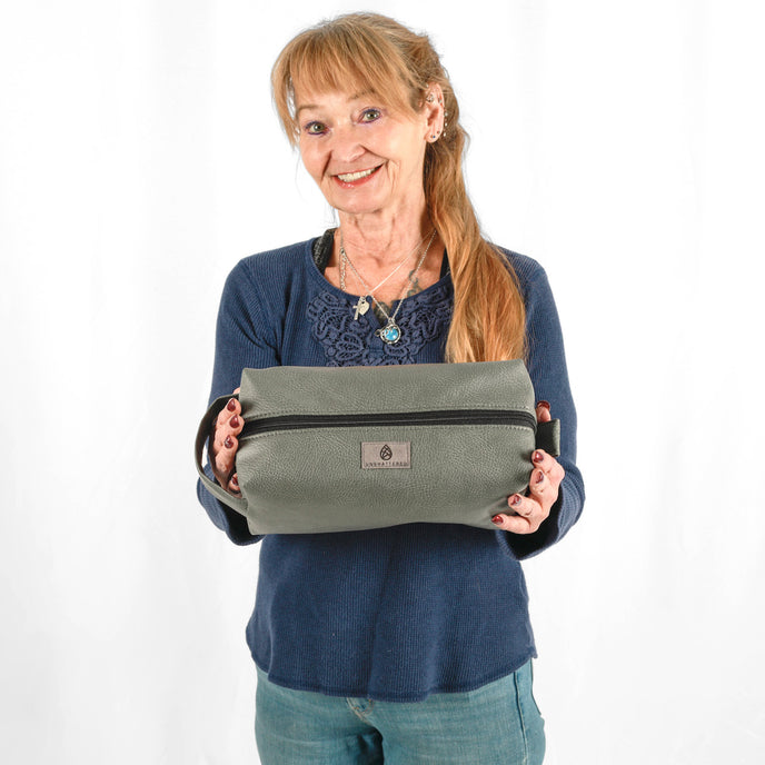 A woman holding a gray luxury leather alternative toiletry kit with a gray label 