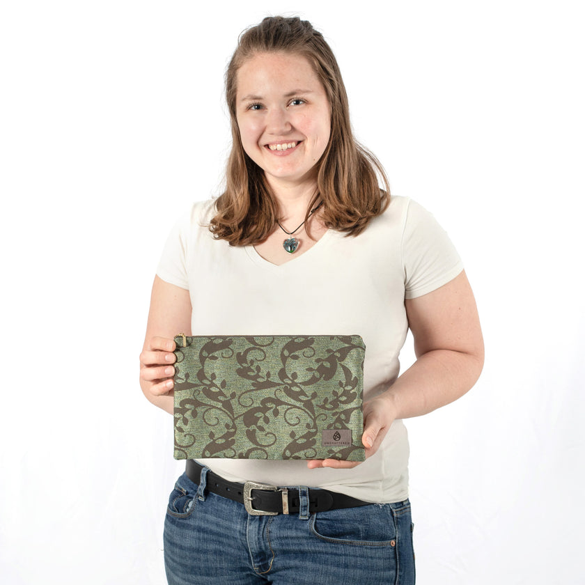 A woman holding a green and brown floral large zip pouch with a gray label  
