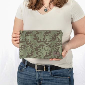A woman holding a green floral zip pouch with gold-tone hardware and gray Unshattered label 