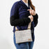 A woman carrying a multicolored tweed crossbody pouch with a zippered top, an adjustable beige strap, and a gold-tone hardware, named after Lydia.