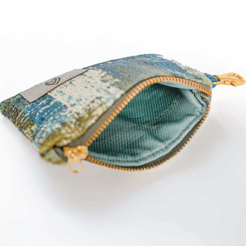 A blue interior fabric with a gold tone zipper on a blue, green and white clip pouch design.
