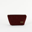 A burgundy floral damask makeup bag with a zip closure and a small brand tag attached to the front named after Alaney 