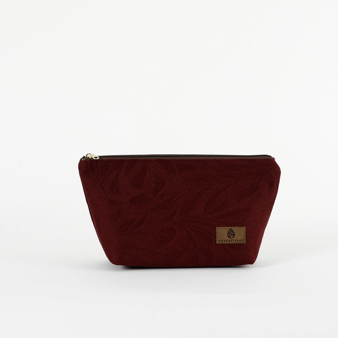 A burgundy floral damask makeup bag with a zip closure and a small brand tag attached to the front named after Alaney 