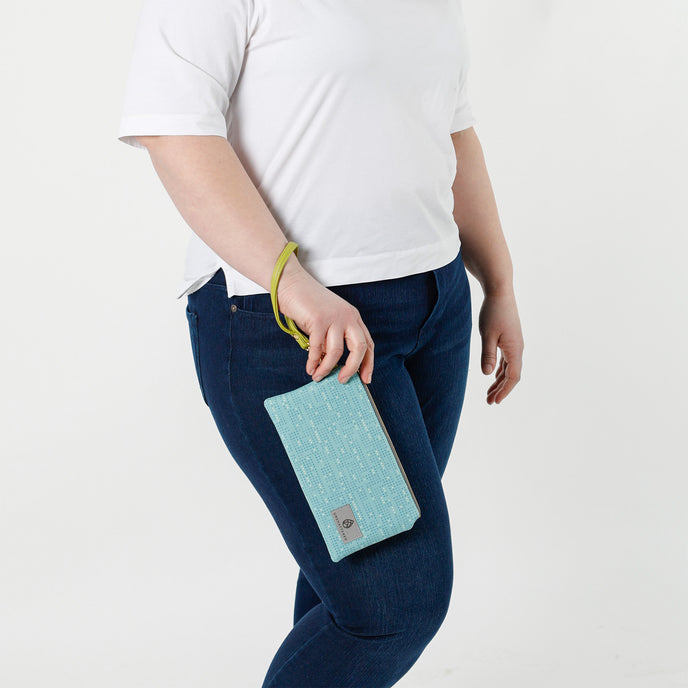 A woman holding a vibrant blue wristlet with dots and a green strap with gold hardware named after Alicia