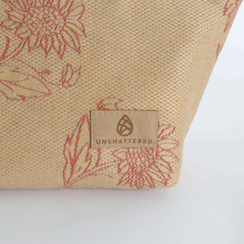Beige fabric with red floral patterns and 'Unshattered' brand logo on a white background