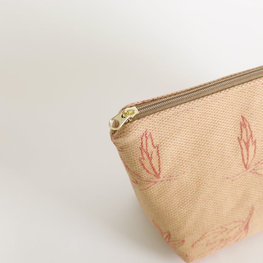Beige makeup kit with red leaf pattern and gold zipper on a light beige background