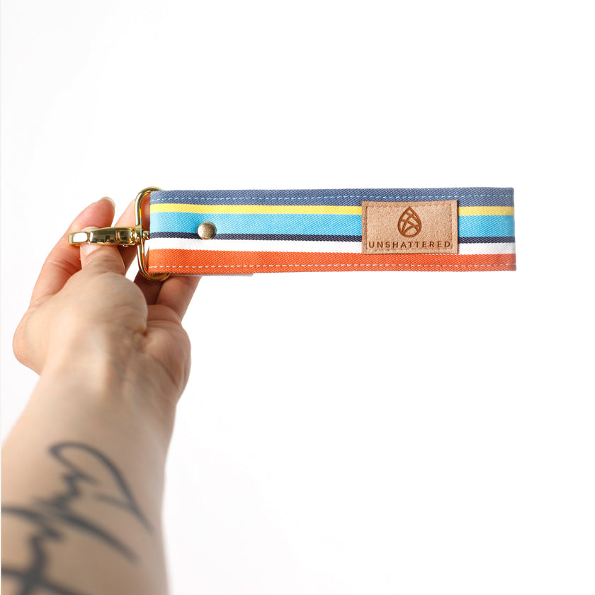 Hand holding a colorful striped key clip with 'Unshattered' branding on a white background named after Angel 