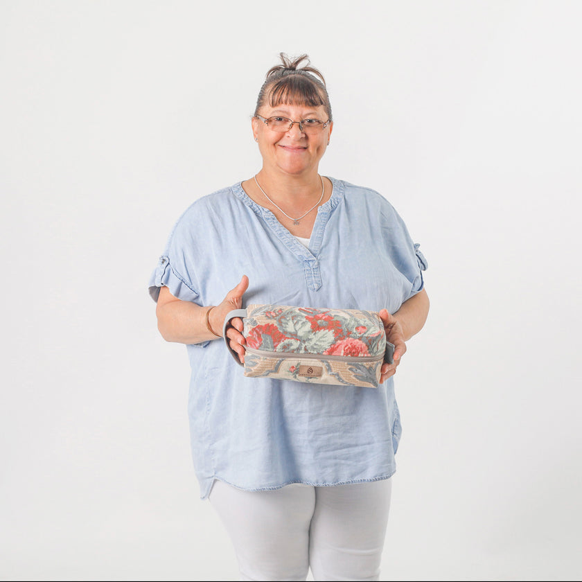 A woman holding a flower toiletry kit wearing a jean colored top with white pants named after Anna 