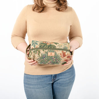 A woman wearing a tan turtleneck with blue jeans holding this beautiful floral and tree toiletry kit 