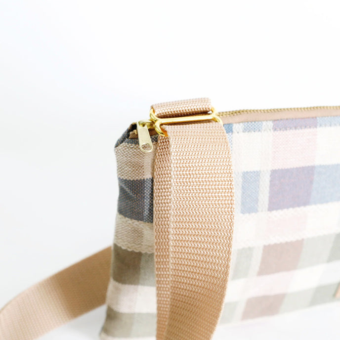 Close-up of a plaid bag with a beige strap on a white background