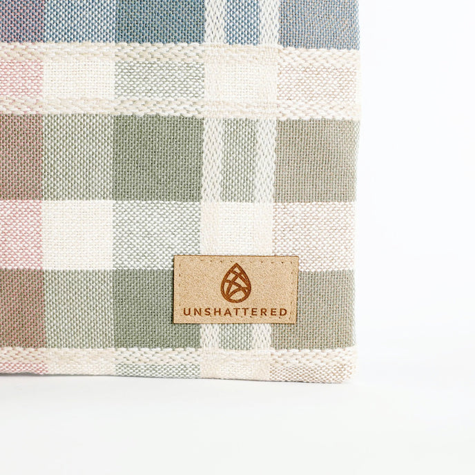 Plaid fabric with a 'Unshattered' logo on a light gray background