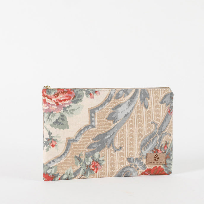 A large zip pouch with a floral design in shades of blue, white, and tan, featuring gold-tone hardware and a Unshattered label named after Ashley 