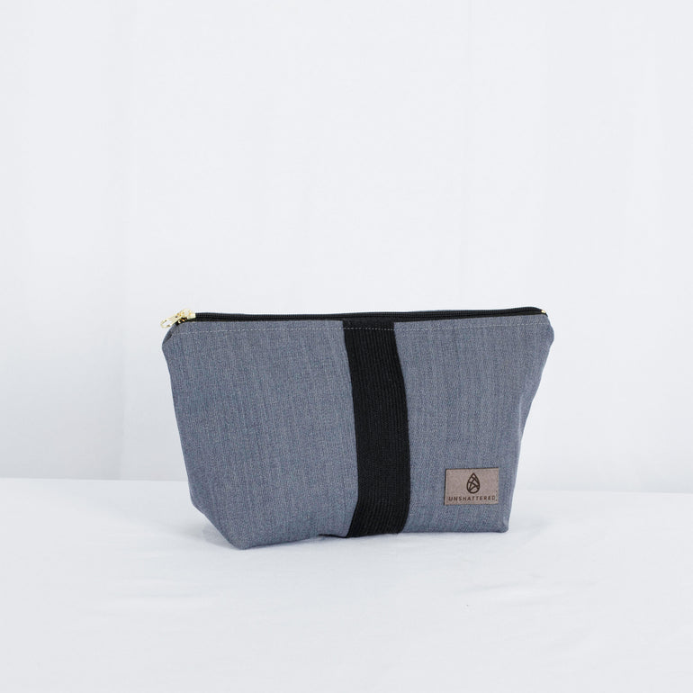 A gray makeup kit with a black zipper and a gold-tone hardware zip closure, made from upcycled West Point Cadet Dress Gray Uniform.