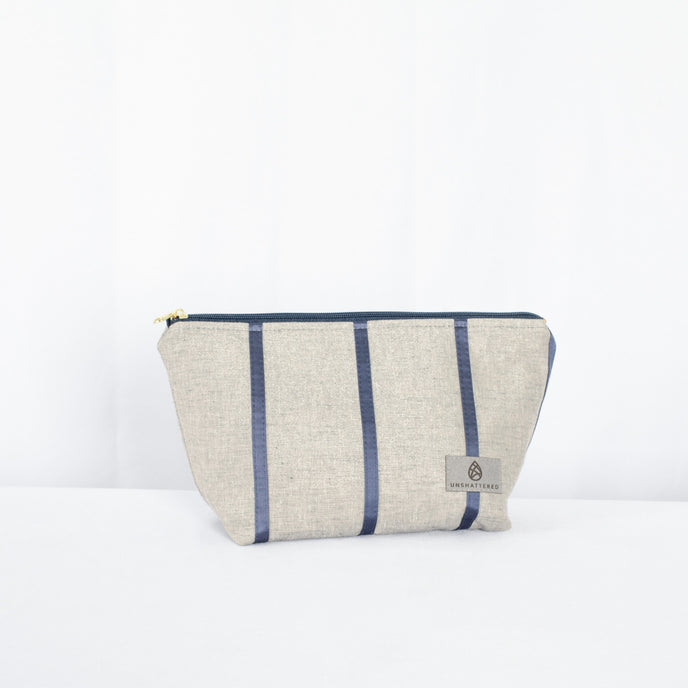 A makeup kit with a gray and blue striped exterior and a blue zipper closure, featuring gold-tone hardware.