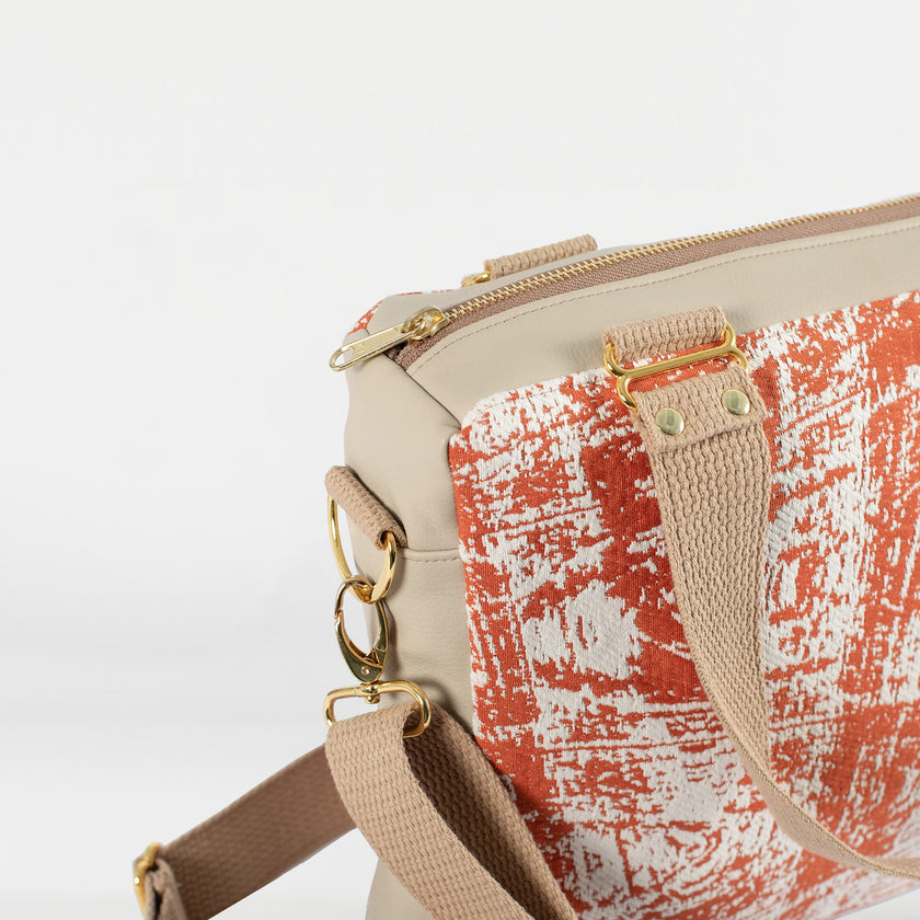 A tan strap with gold hardware on an orange and white handbag 