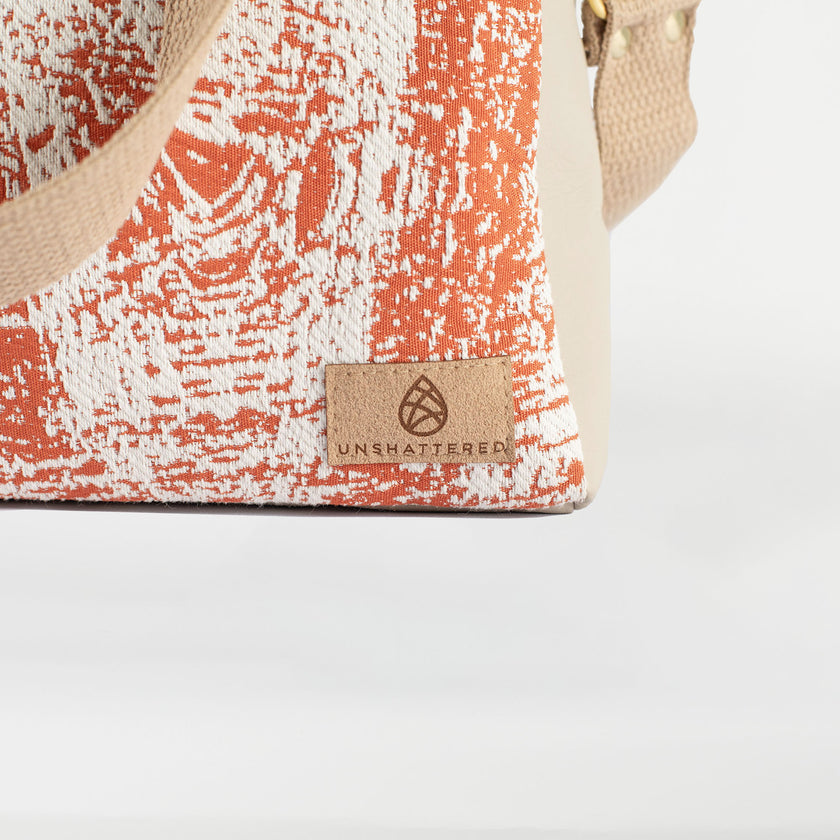 A tan label on an orange and white handbag with a tan strap 