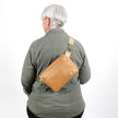 Person wearing a tan crossbody bag on a white background