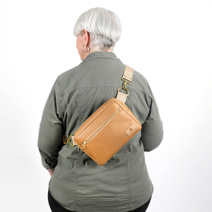 Person wearing a tan crossbody bag on a white background